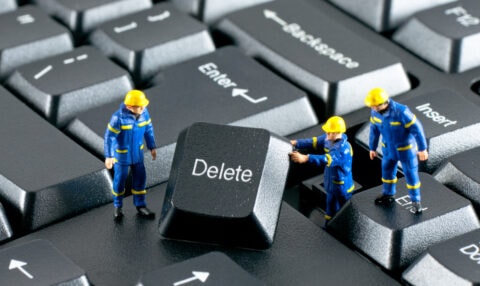A group of construction workers standing on a keyboard with the word delete.