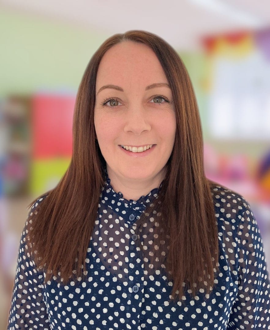 A woman in a polka dot shirt standing in a classroom.
